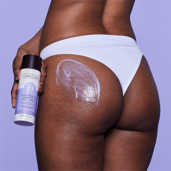 A close-up of a person from the back wearing white underwear, holding a can of Frank Body Regenerating Healing Body Cream with a thick white cream swatch applied to the upper buttock against a solid lavender background.