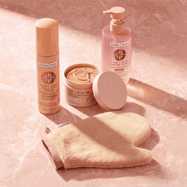 The frank body Bronze With Benefits Kit products and tanning mitt arranged on a pink marble surface.