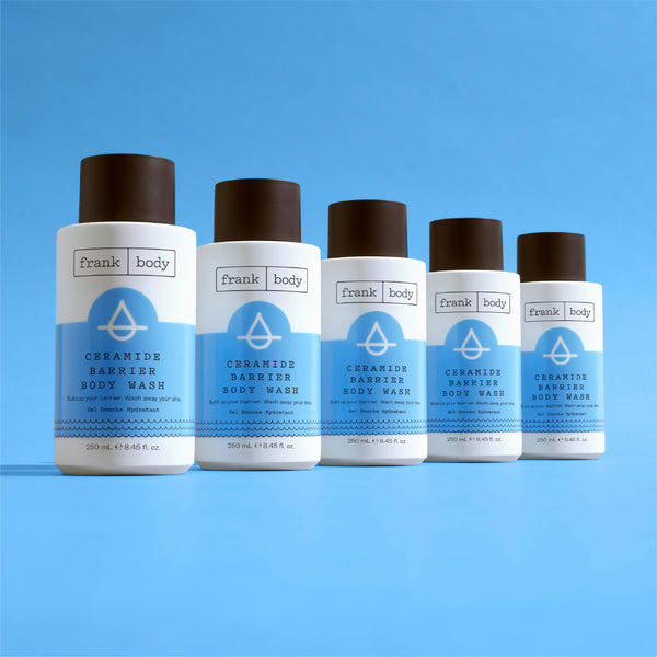 Five bottles of frank body Ceramide Barrier Body Wash lined up on a blue background.