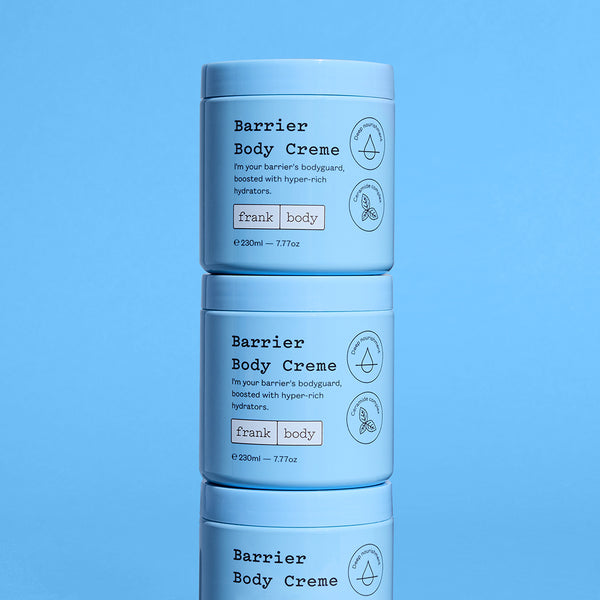 Three stacked light blue plastic jars of frank body Barrier Body Creme against a solid blue background.
