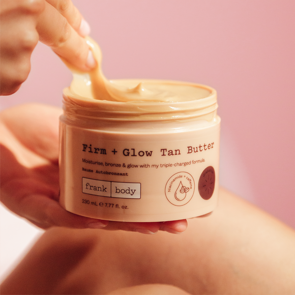 A hand scooping frank body Firm + Glow Tan Butter from its open tub.