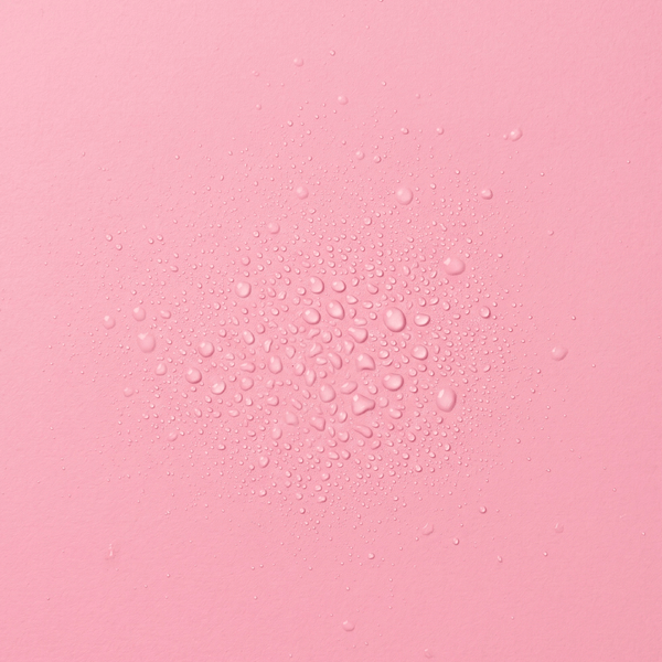 Droplets of frank body Hot Lick Hair & Body Mist on a pink background.