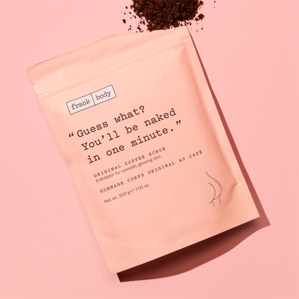 A pink stand-up pouch of Frank | Body Original Coffee Scrub with a humorous quote printed on the front, styled on a matching pink background with coffee grounds scattered at the top.