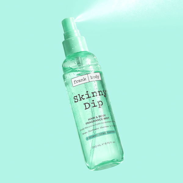 A bottle of frank body Skinny Dip Hair & Body Mist spraying against a mint background.
