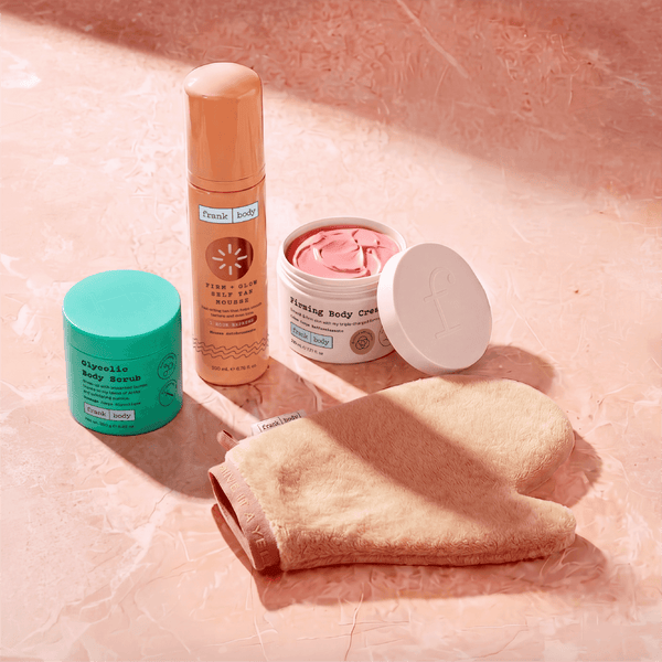 The frank body Everything Shower Kit products and tanning mitt arranged on a pink marble surface.