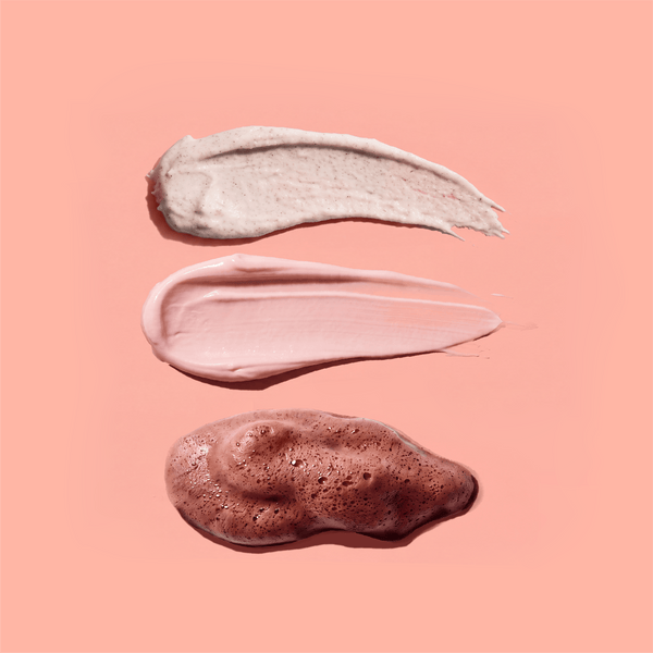 Swirls of frank body Gentle Body Scrub, Firming Body Cream and Self Tan Mousse on a pink background.